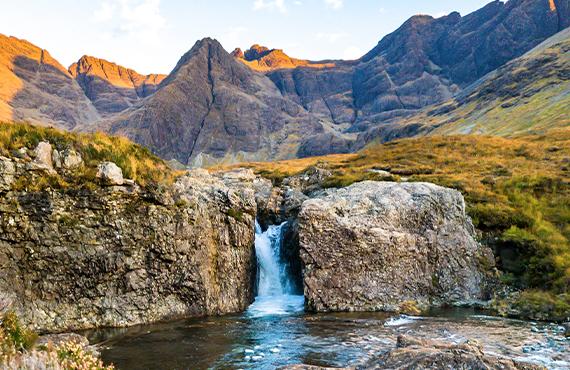 A small waterfall flowing into a river on the Isle of Skye's mountainous terrain.