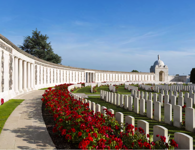 Tyne Cot Commonwealth War Graves Cemetery, Ypres, with blue sky and red flowers 