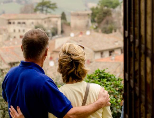 middle aged couple facing with backs to camera and arms around one another looking out over an Italian village skyline
