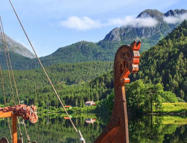 replica of a Viking ship docked in a Norwegian fjord surrounded by woodland and mountains