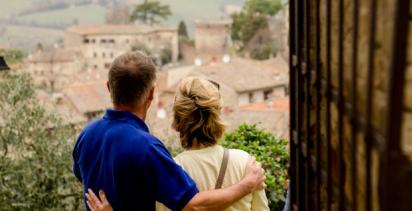 middle aged couple facing with backs to camera and arms around one another looking out over an Italian village skyline