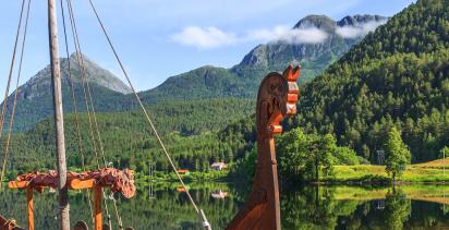 replica of a Viking ship docked in a Norwegian fjord surrounded by woodland and mountains