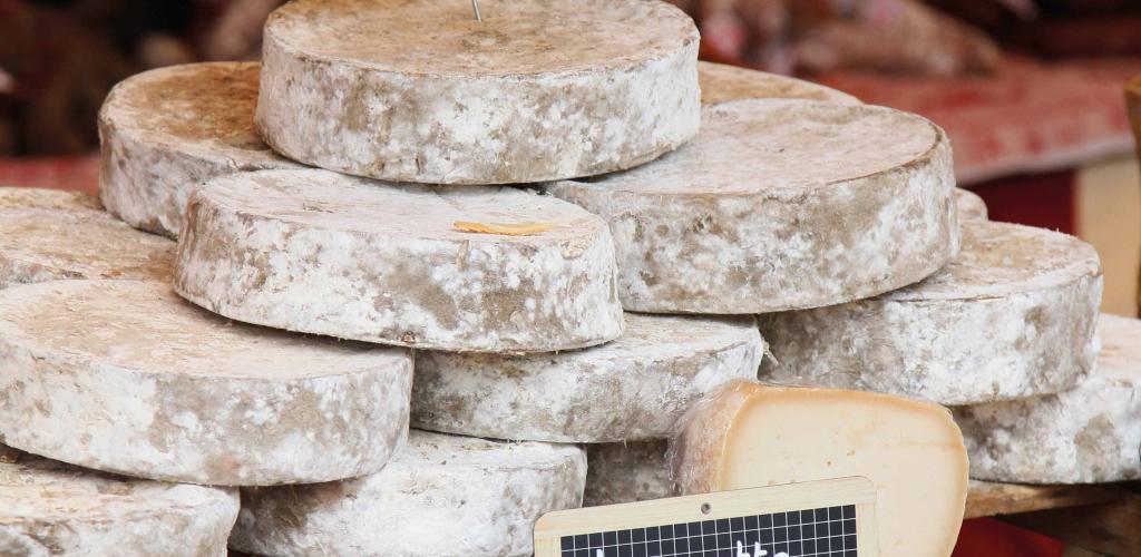 rounds of various french cheeses stacked on market stall bench