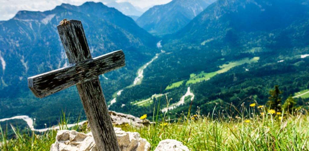 cross of christ perched up on green hill overlooking valley