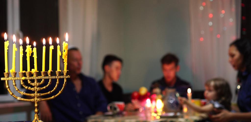 family sitting at table celebrating hanukkah with menora in foreground