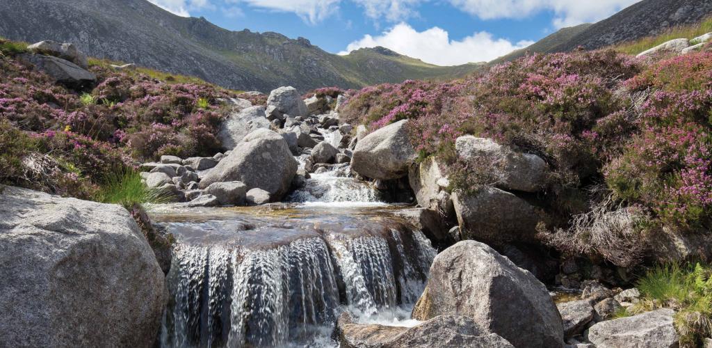 cascading waterfall over grey rocks with rolling hills in the background
