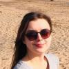 young woman with dark hair and sunglasses with a sandy background